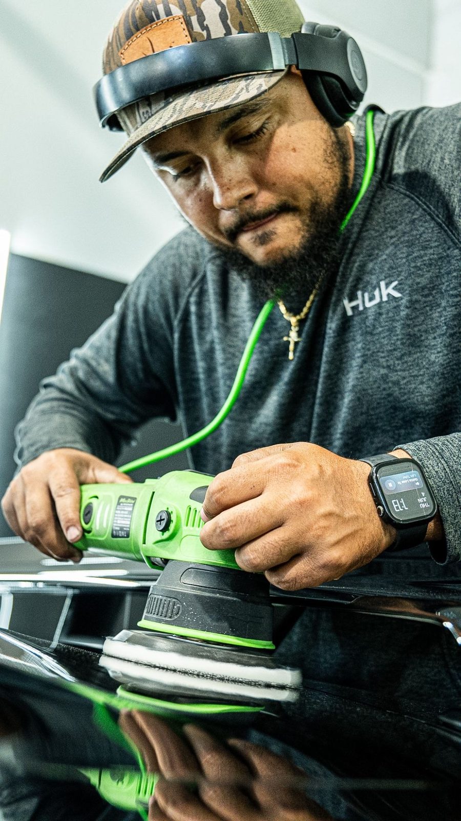 Detailer running a green polisher on black paint